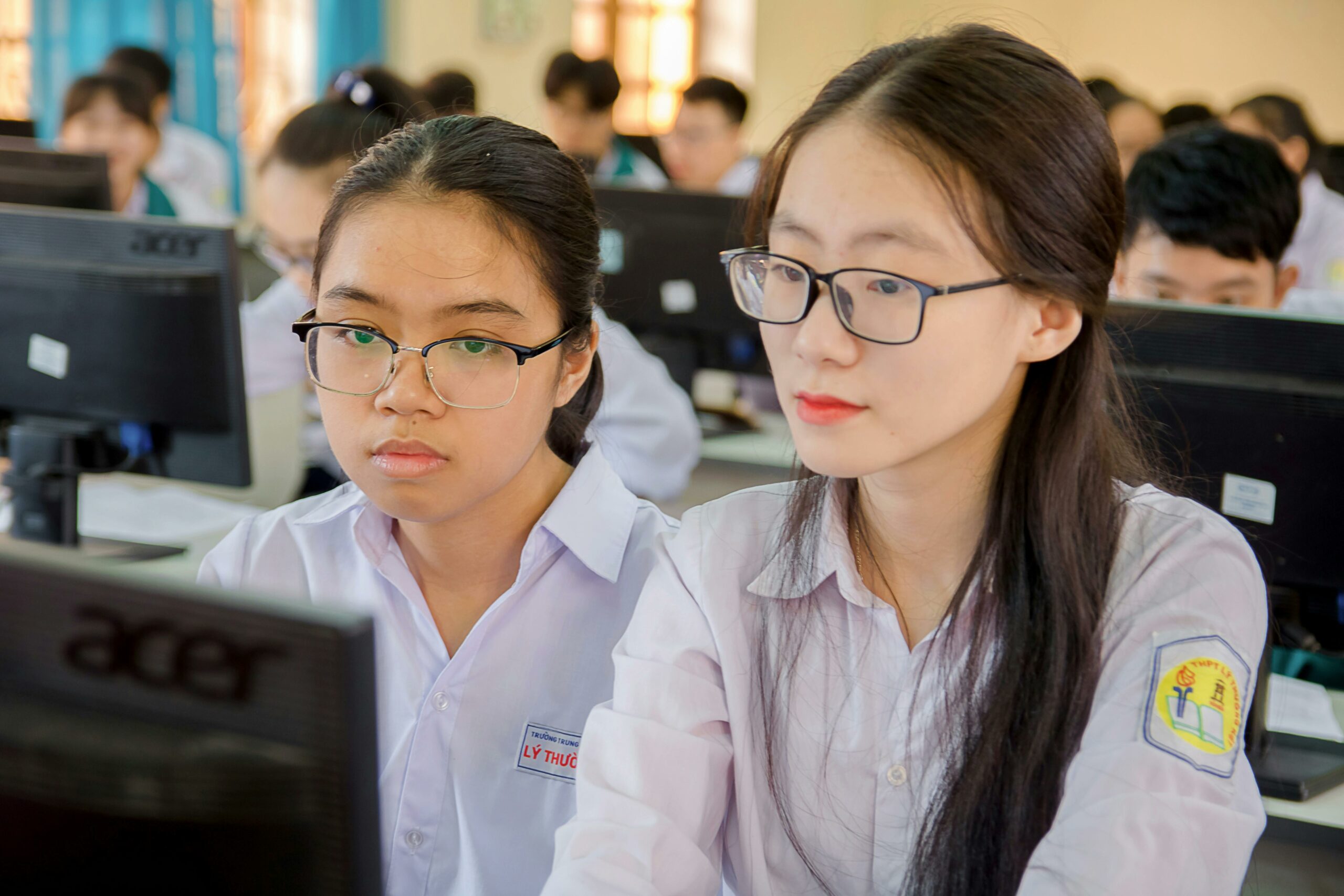 Two female students in a classroom focusing on computer work, showcasing education and technology.